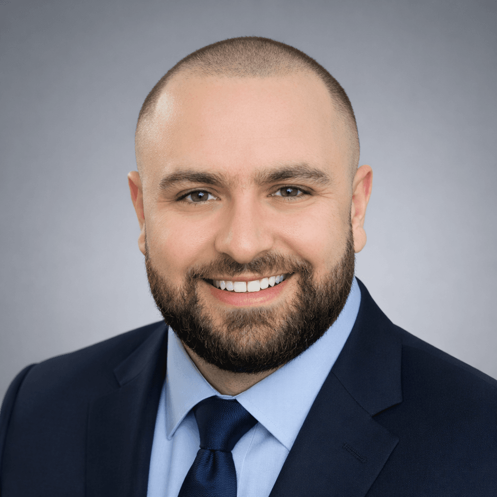 Professional headshot of a smiling man with a shaved head, beard, and blue suit.
