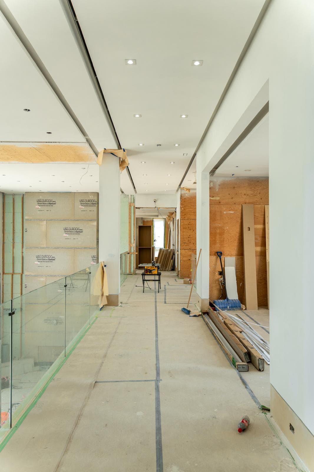 Modern hallway under construction with white ceilings, recessed lights, unfinished walls, and scattered building materials.