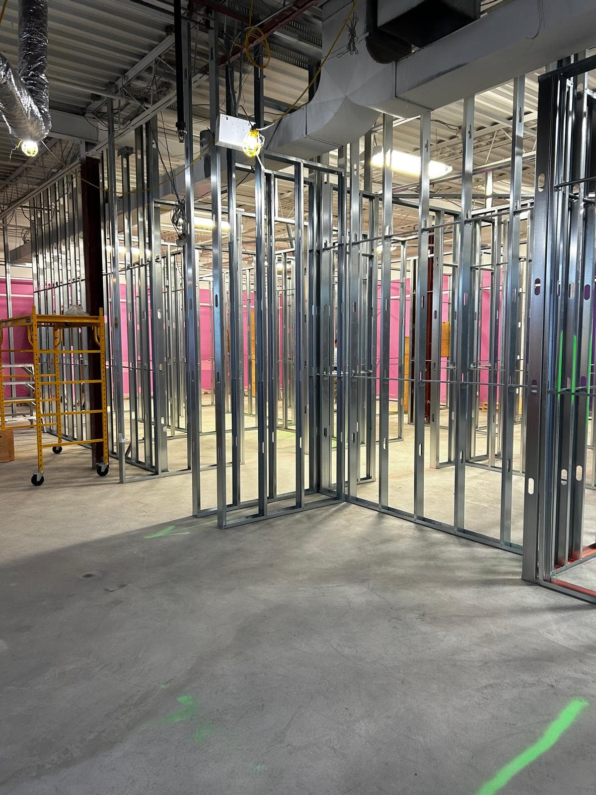 Interior construction site featuring metal wall framing, concrete floors, and a yellow rolling scaffold.