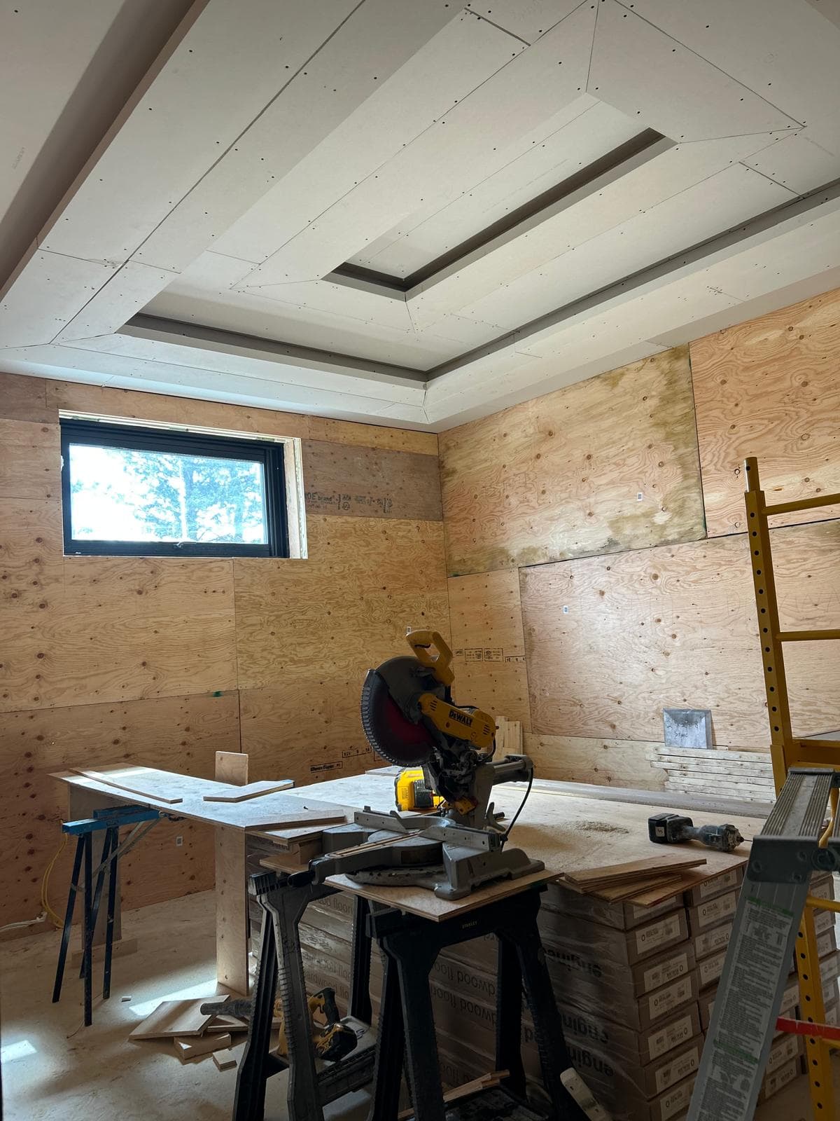 Plywood-walled room under construction with a recessed tray ceiling and a miter saw.